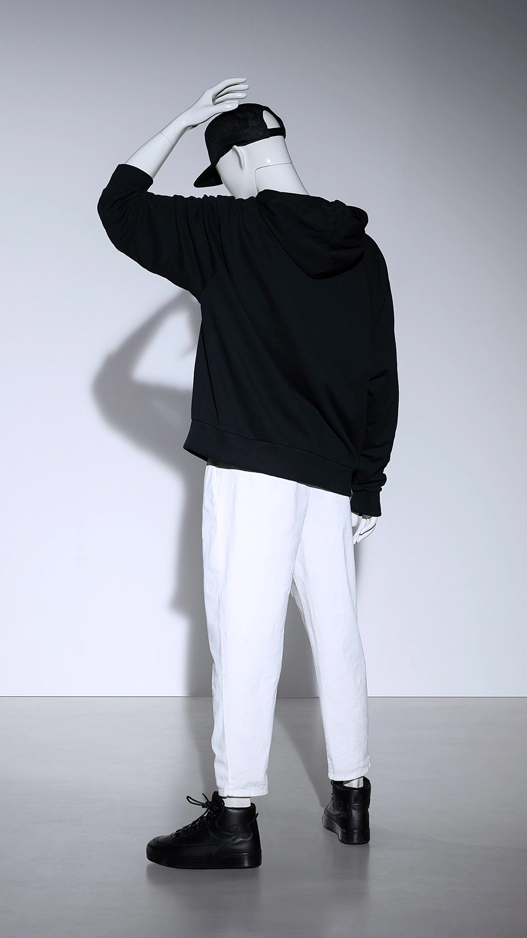 a male mannequin from the blend collection standing with his back towards the camera, his hand on his head and wearing a black hoodie and white pants